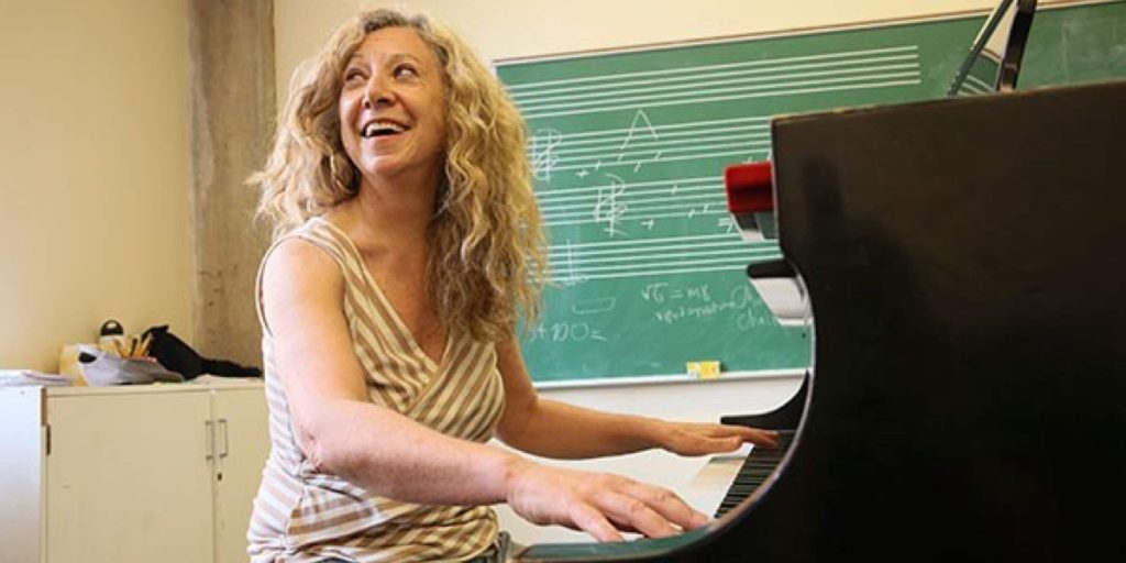 woman smiles while playing piano in a classroom