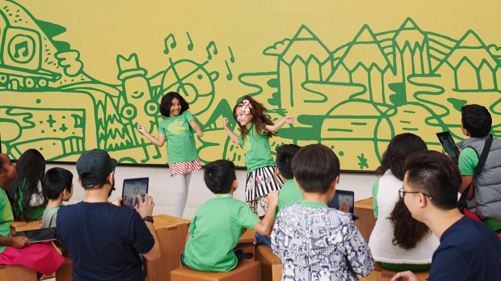 two children dance in front of a group of other children in apple branded tee shirts