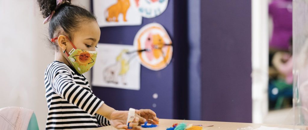young girl doing crafts at a table wearing a face mask