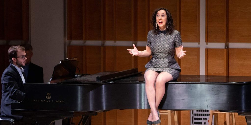 Gabrielle Stravelli sitting on a piano and singing