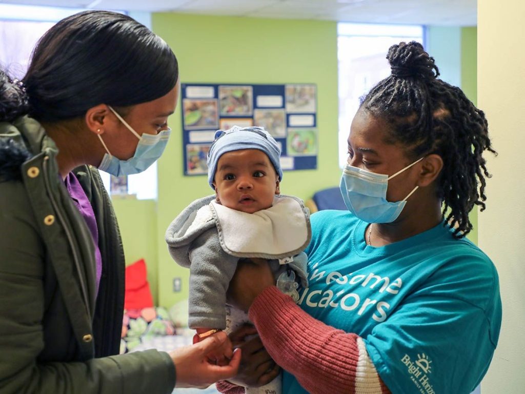 child care professional wearing a mask holding a baby