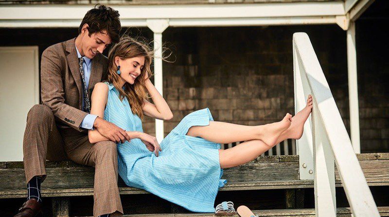 man and woman sit on the steps of a beach house in summer clothes from Brooks Brothers