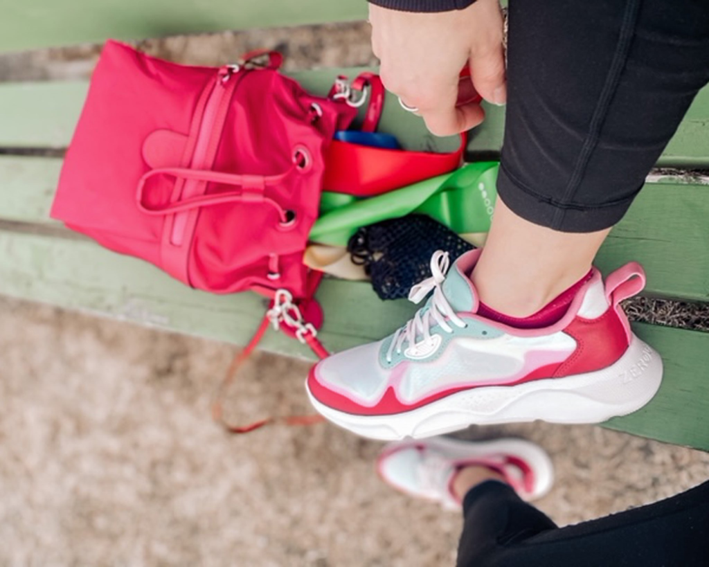 close up of a pink running sneaker on a woman's foot propped up on a bench near her backpack