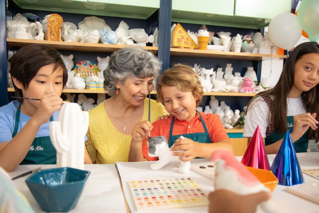 An older woman helps a young boy paint a piece of pottery at a color me mine studio