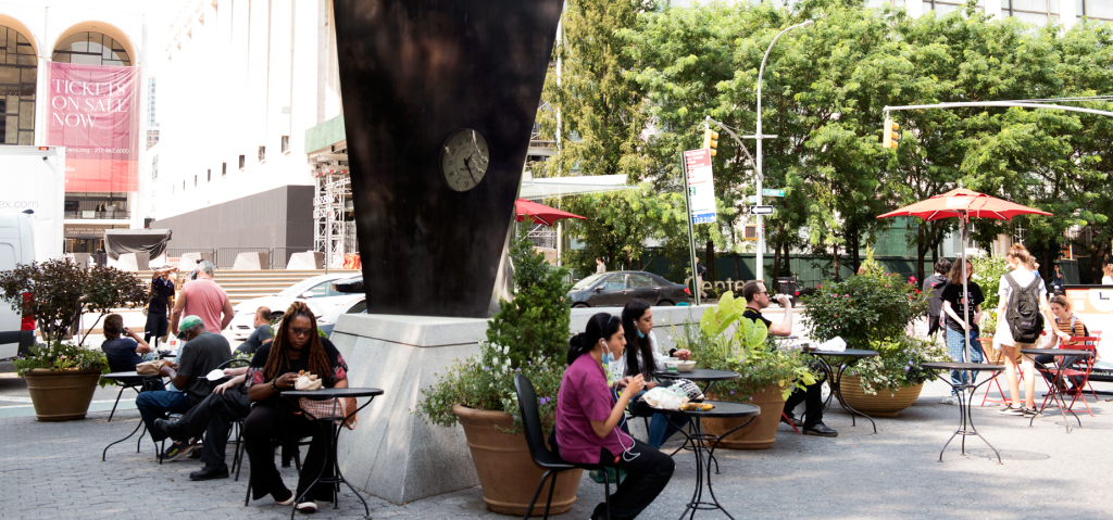 people sit at the tables and chairs provided by the LSBID around the movado clock in dante park