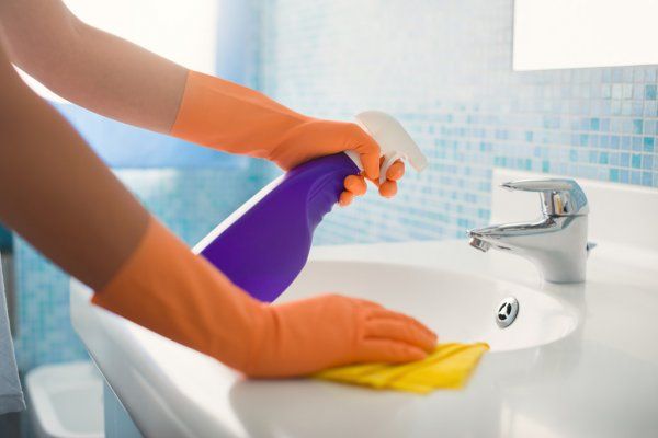 a person's hands wearing rubber cleaning gloves wipes down a sink counter with a rag and cleaning spray
