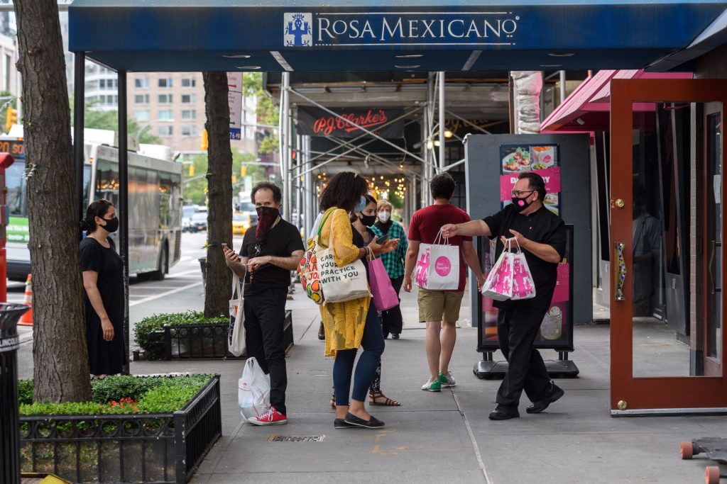 people wait outside for take-out at Rosa while one employee hands a bag to a customer