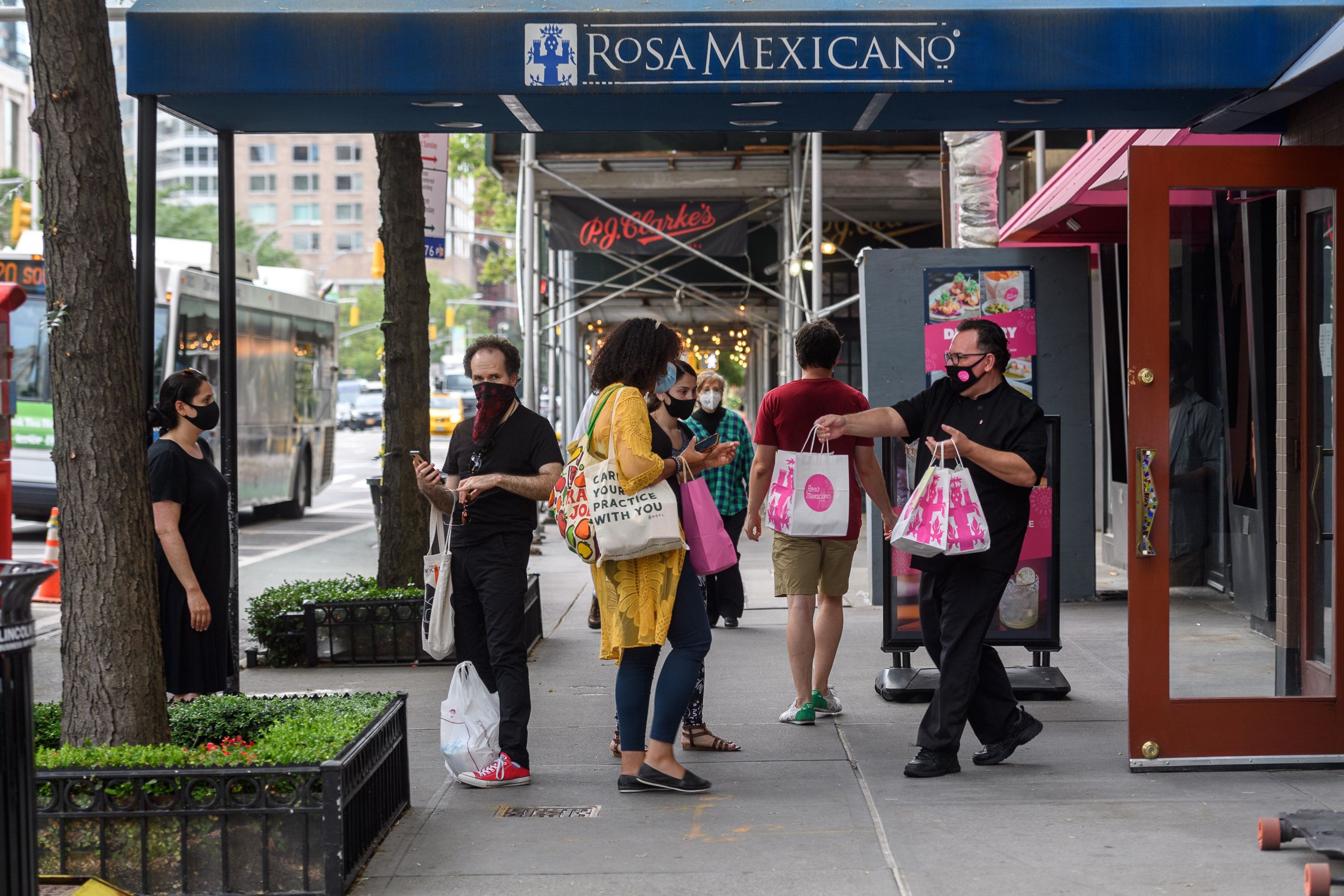 people wait outside for take-out at Rosa while one employee hands a bag to a customer