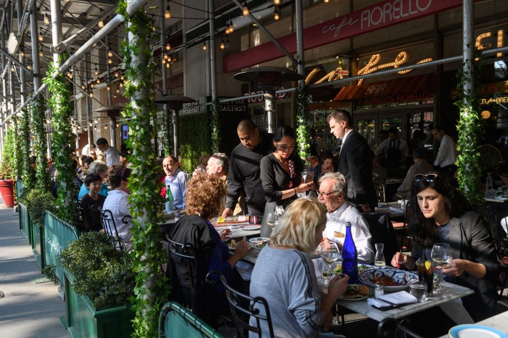 People dine in an outdoor seating area on Broadway in the summertime