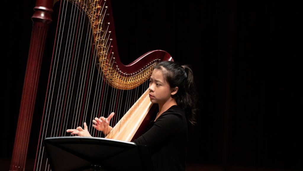 Juilliard musician plays the harp against a black background