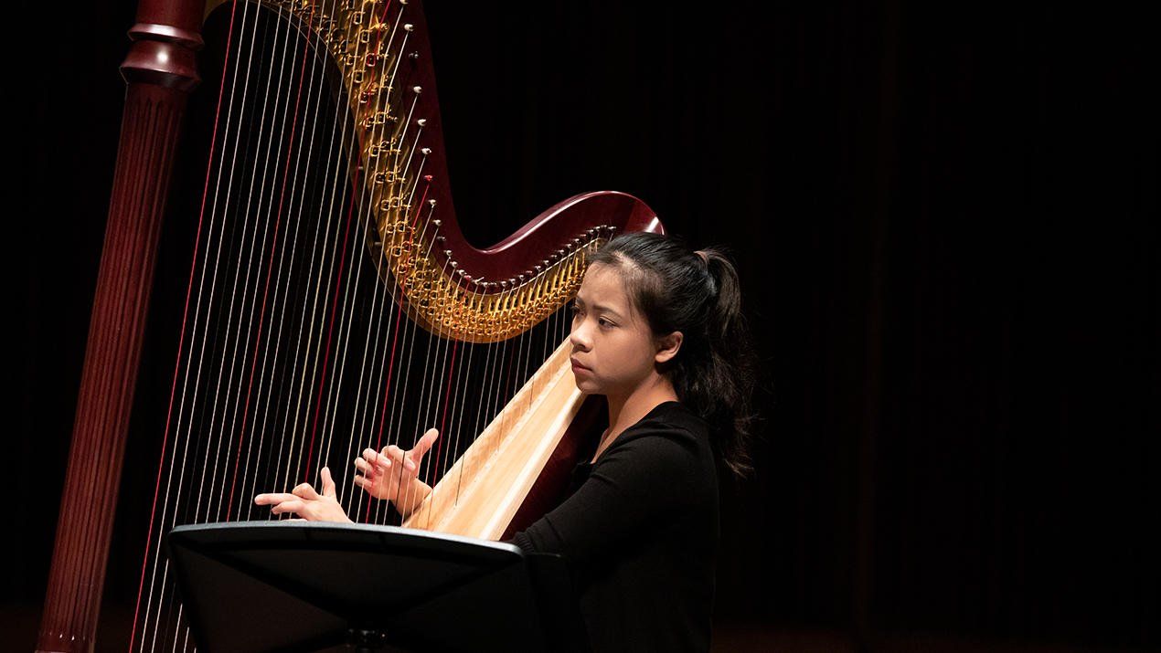 Juilliard musician plays the harp against a black background