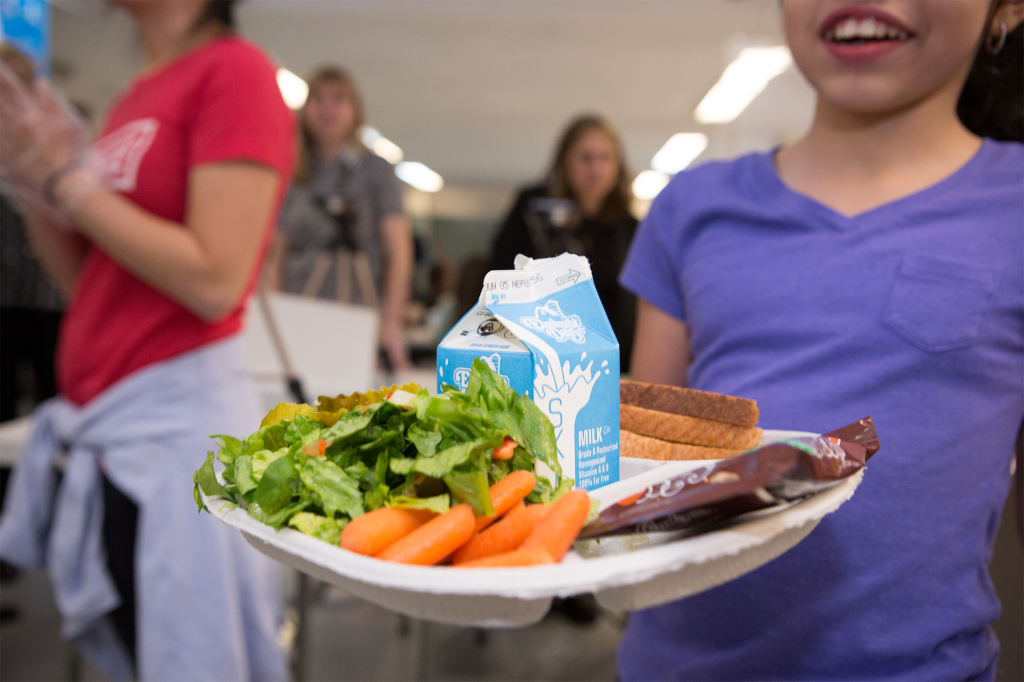 a young girl holds a plate of food from a meal hub