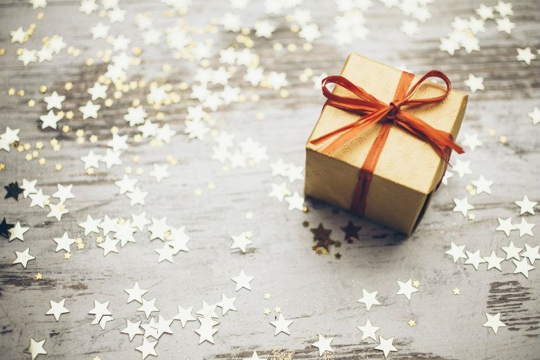 brown paper wrapped gift box with a red ribbon on a table surrounded by cutout stars