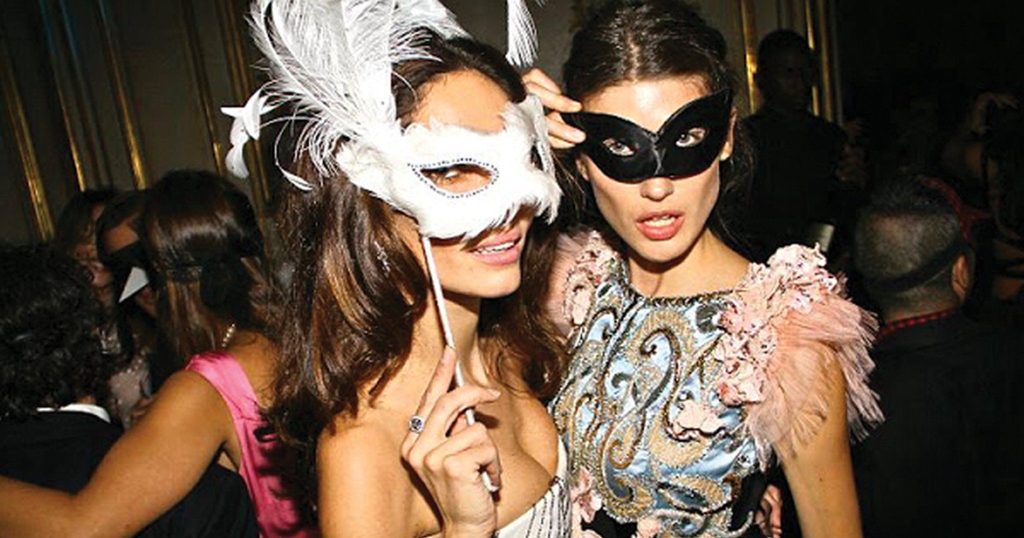 two young women wear masquerade masks at a party