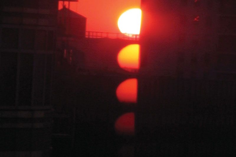 a red sun glares over some city buildings in the evening