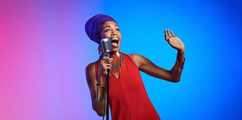 Jazzmeia Horn sings into a mic with a blue and purple background