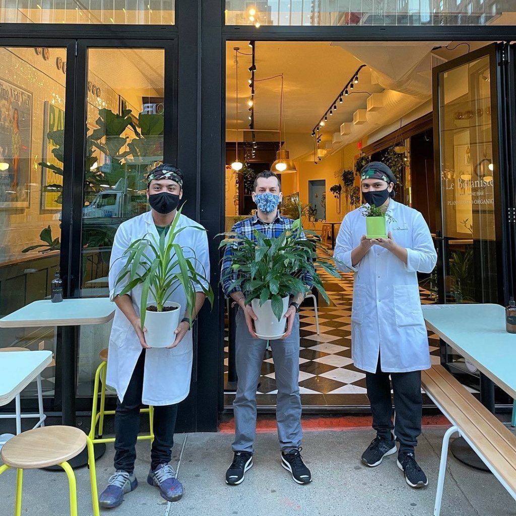 three young employees from Le Botaniste Upper West Side pose in front of the restaurant with plants