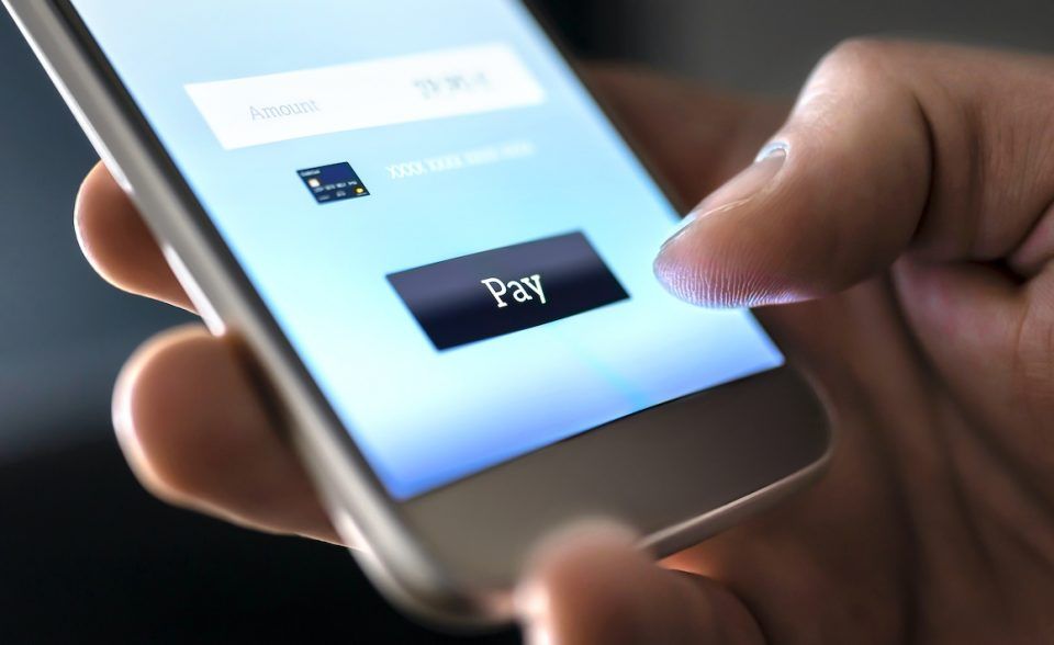 a hand holds a smartphone intending to press a purchase button through an online bank