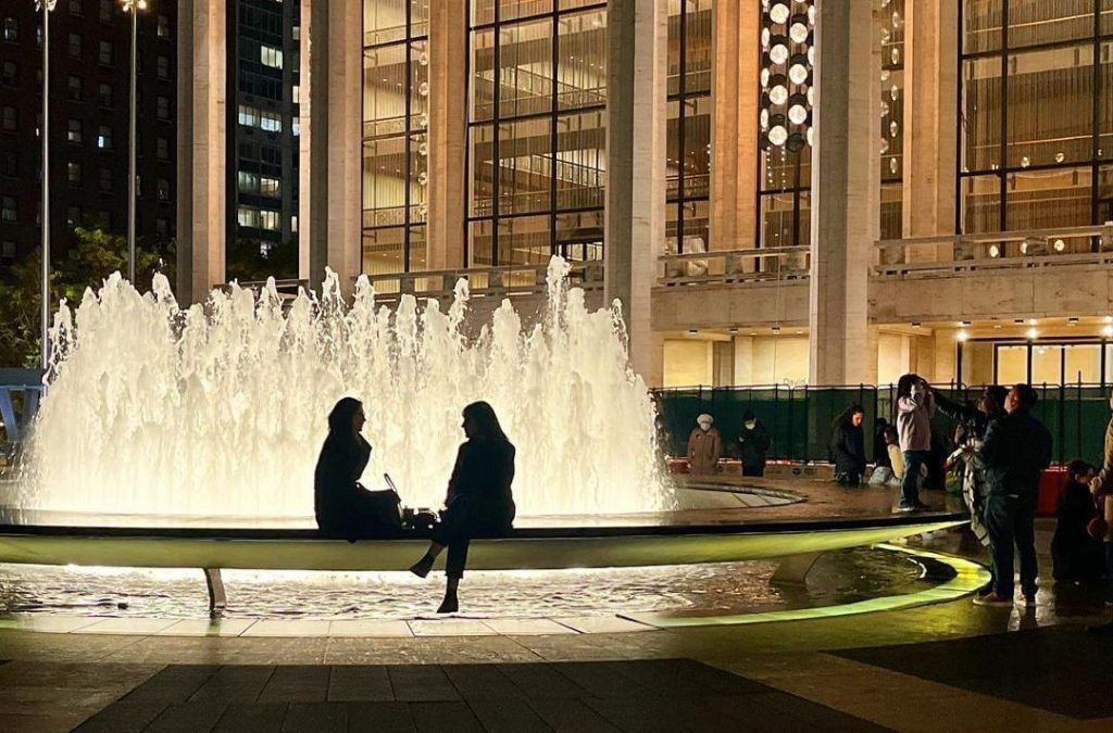 Two shadowed individuals sit on the Lincoln Center fountain facing each other