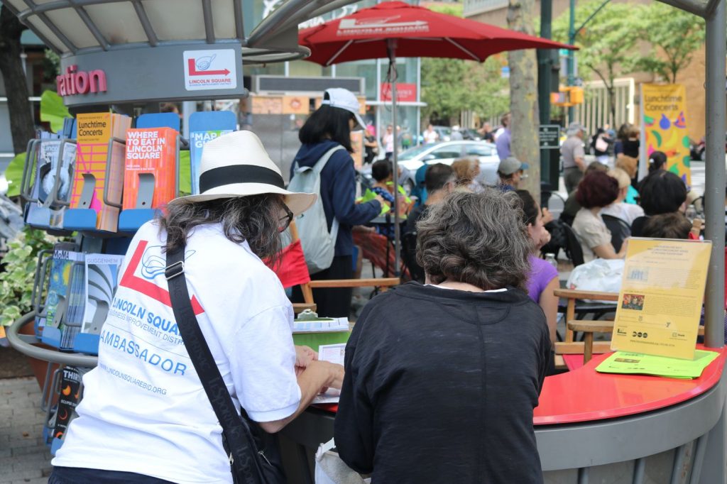 An Information Ambassador points out directions on a map to a visitor in Richard Tucker Park