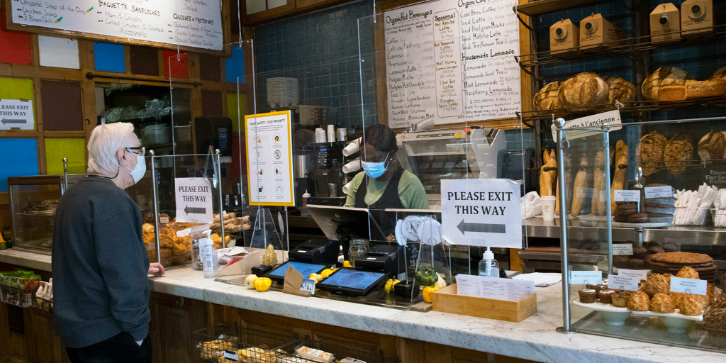 a person in a fleece and a white masks orders from the cashier at Le Pain Quotidien