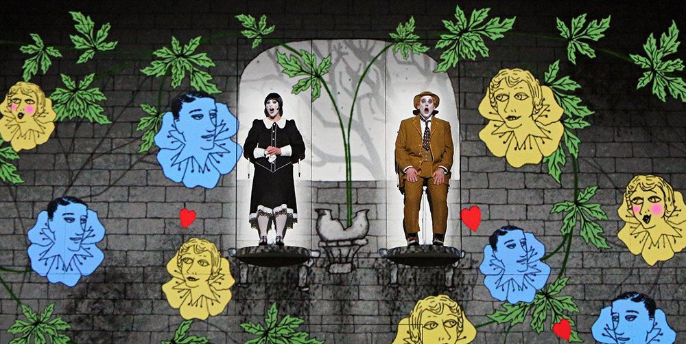 two actors on stage with a CGI background of vines