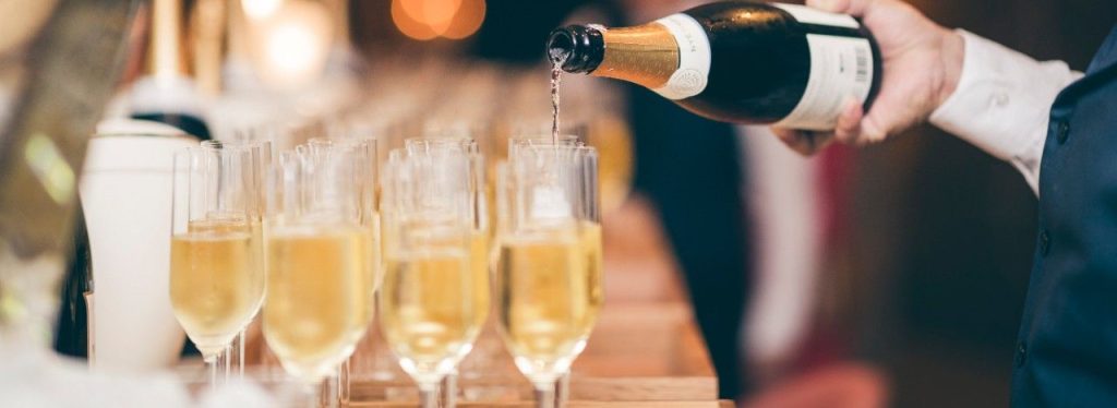 a waiter pours champagne into a row of glasses on a wooden bar top