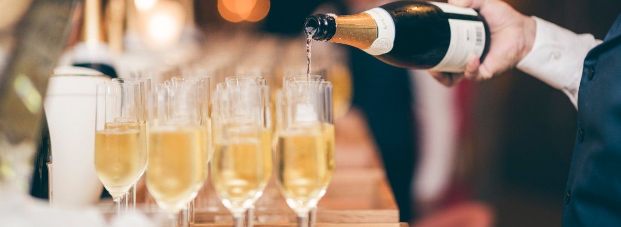 a waiter pours champagne into a row of glasses on a wooden bar top