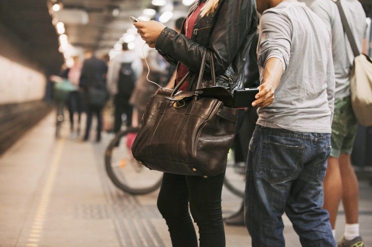 a man's arm pulls a wallet from a woman's bag who is waiting on the subway platform