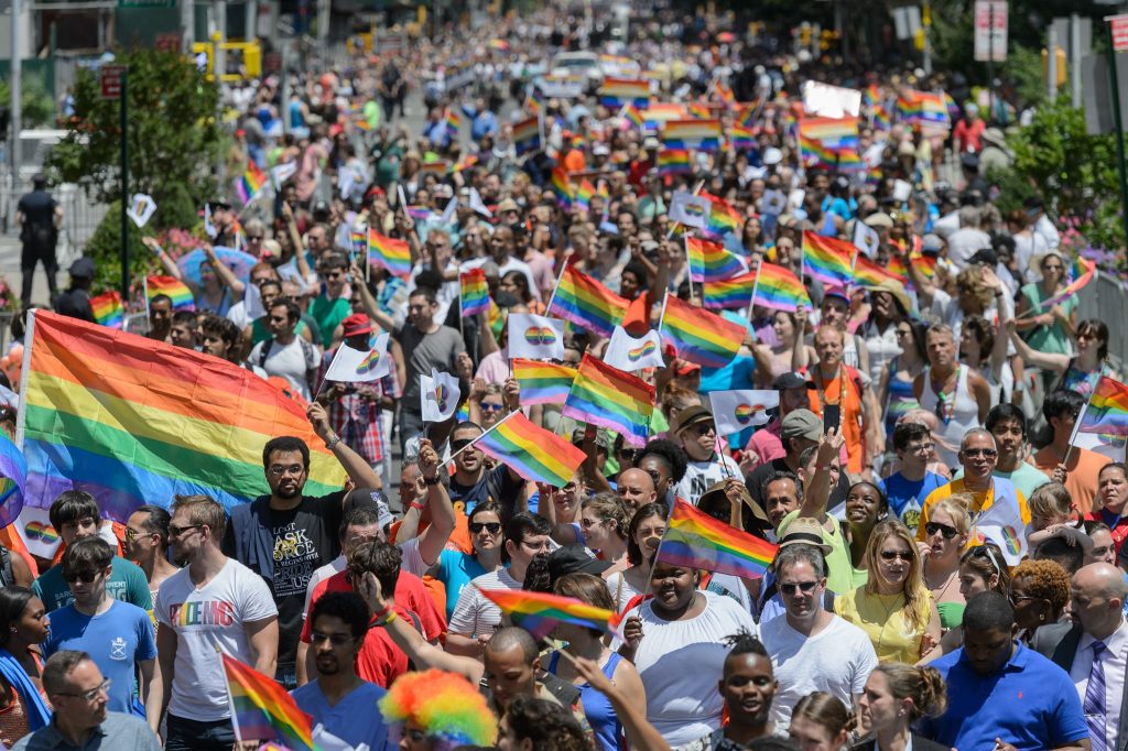 A large crowd of people march for Pride with rainbow flags