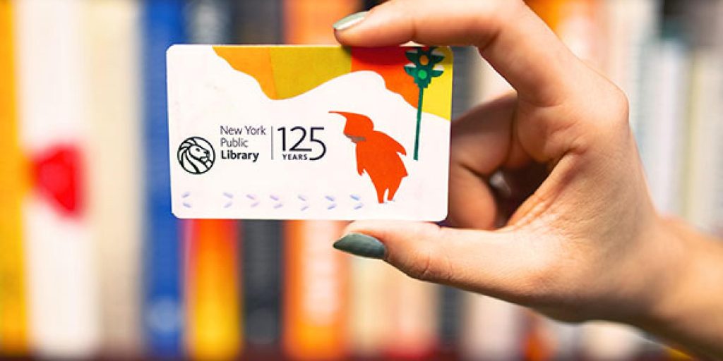 a hand with blue painted nails holds up a special edition library card for the 125th anniversary of the new york public library