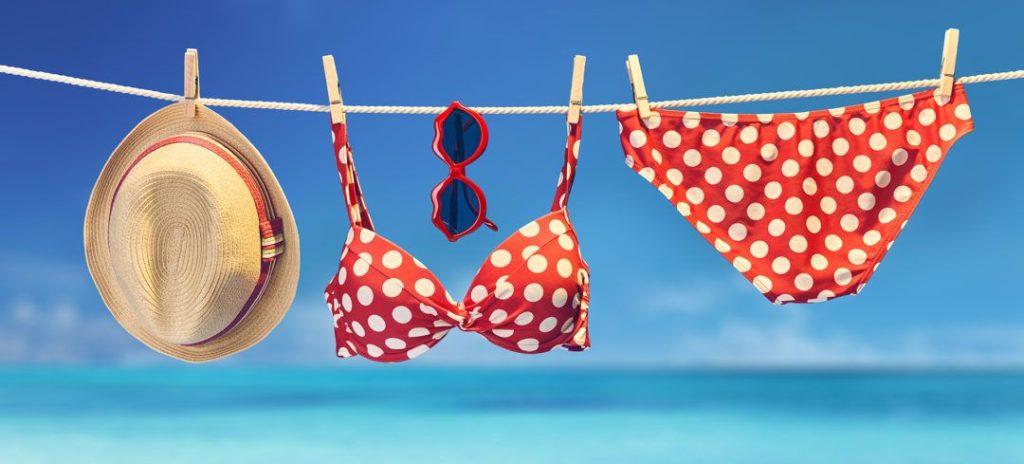 red bikini hangs on a clothesline with sunglasses and a straw sun hat at the beach