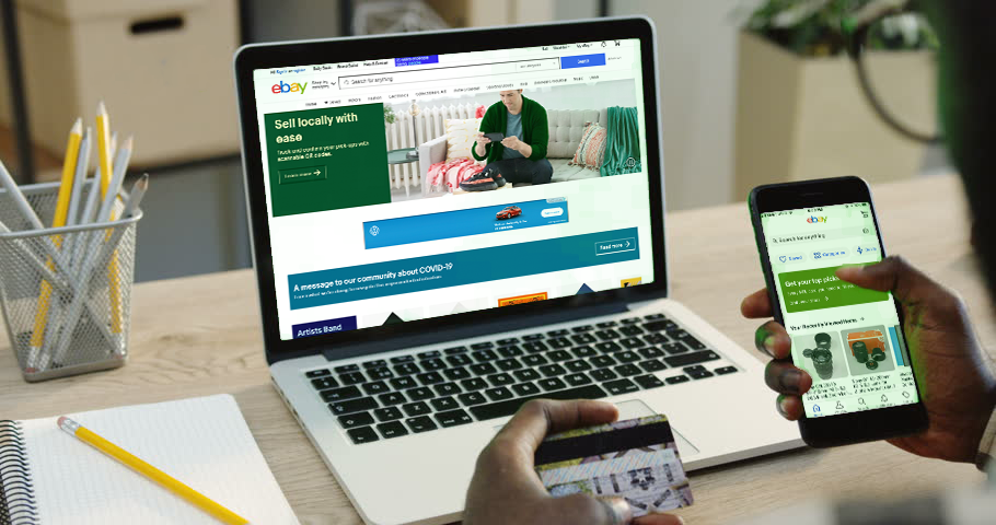 an older gentleman uses his credit card to access ebay on his laptop. we see this from over his shoulder.