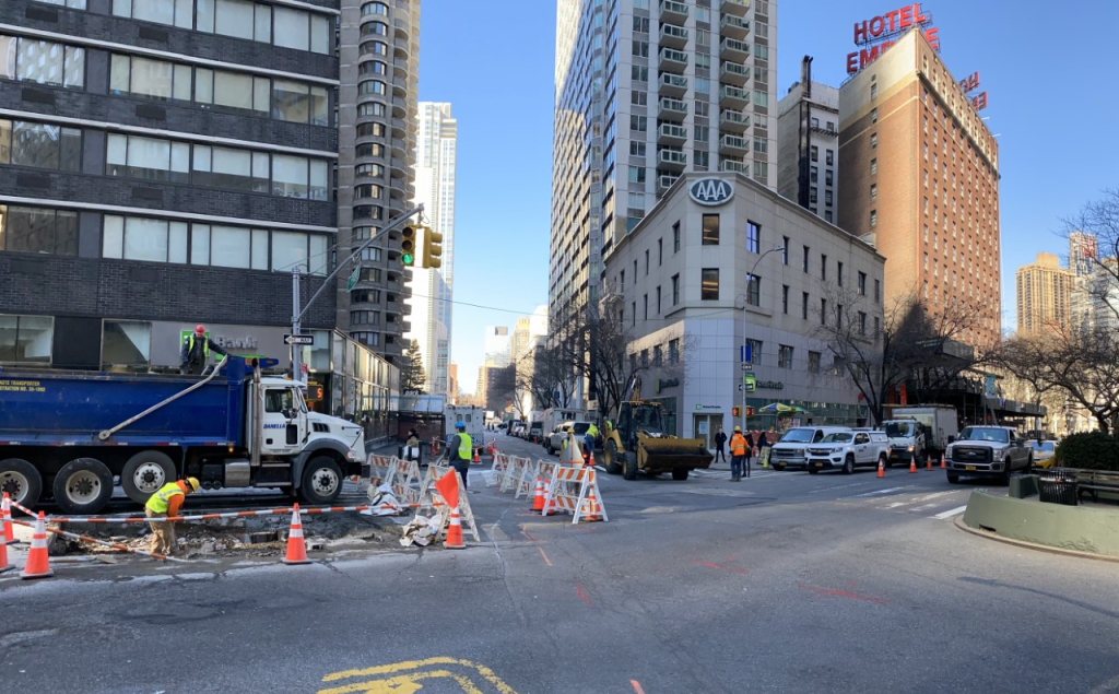 looking down West 62nd St towards Columbus Ave from Broadway with construction trucks and cones on the street