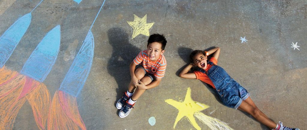 two kids laying on the pavement with chalk drawings around them
